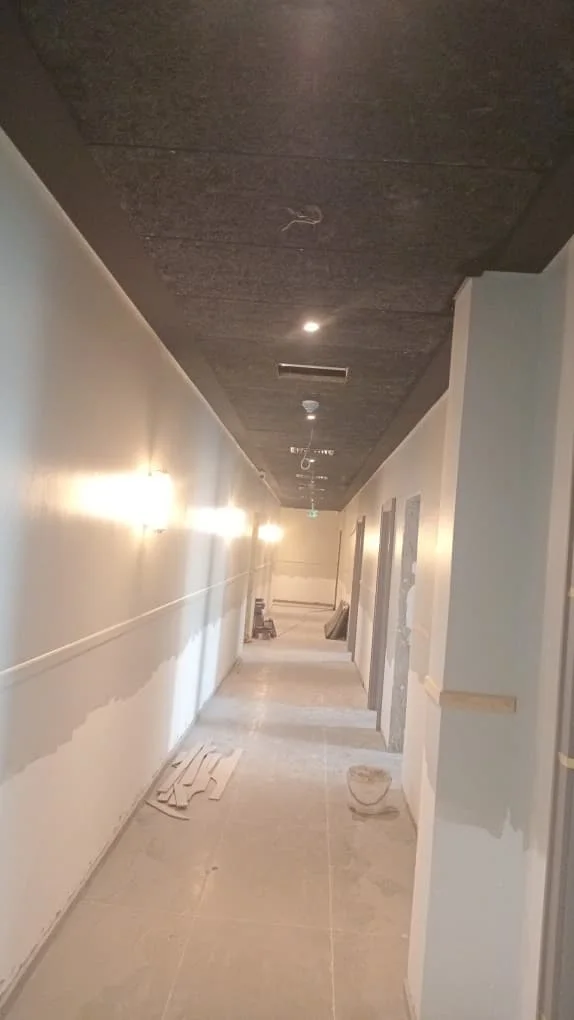Long hotel corridor with a dark ceiling, recessed lights and partly painted pale walls