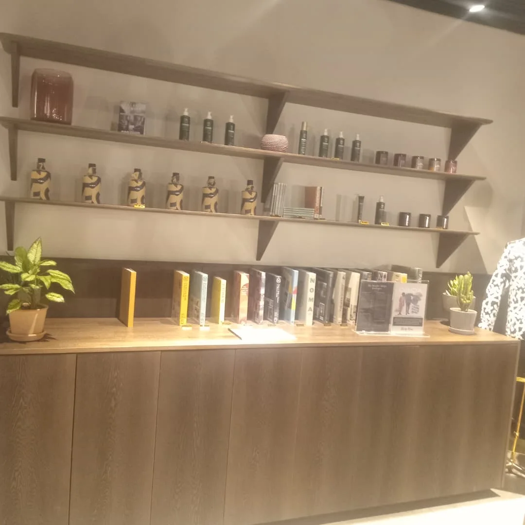 Timber display unit with shelves of ornaments, bottles and books beside a potted plant