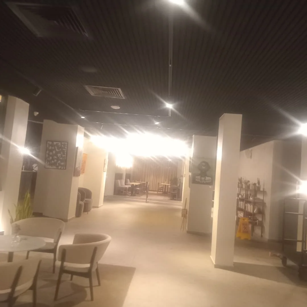Open hotel lobby with a dark slatted ceiling, columns and a dining area in the distance