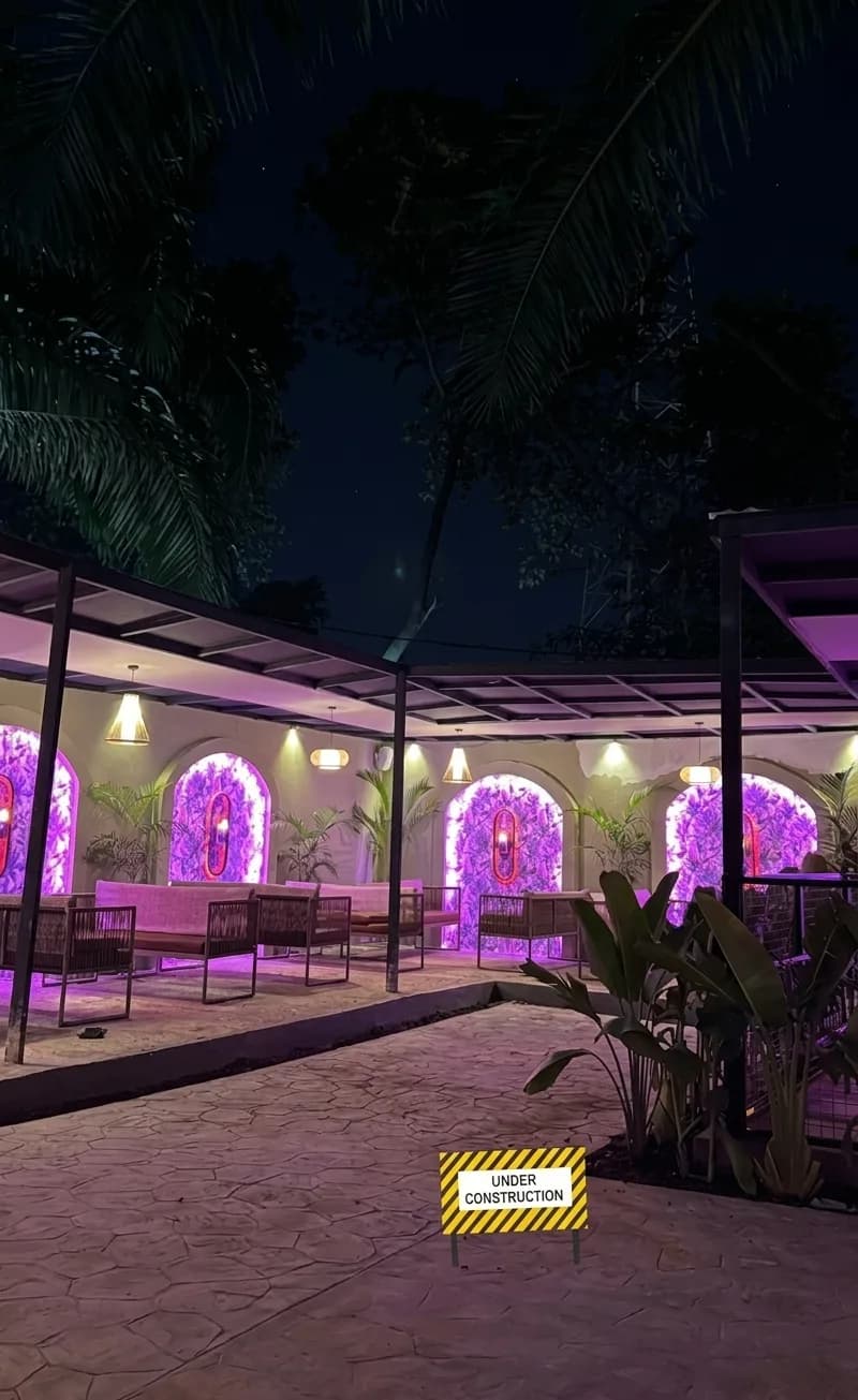 AI-generated image: courtyard terrace at night with pink-lit arched niches, planting and a canopy